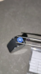 Blue gemstone held by tweezers on a dark background