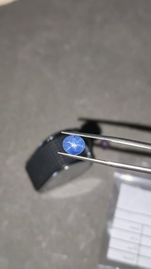 Blue gemstone held by tweezers on a dark background